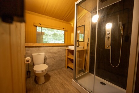 De safaritent heeft een badkamer met een toilet, een wastafel en een douchecabine met een regendouche.